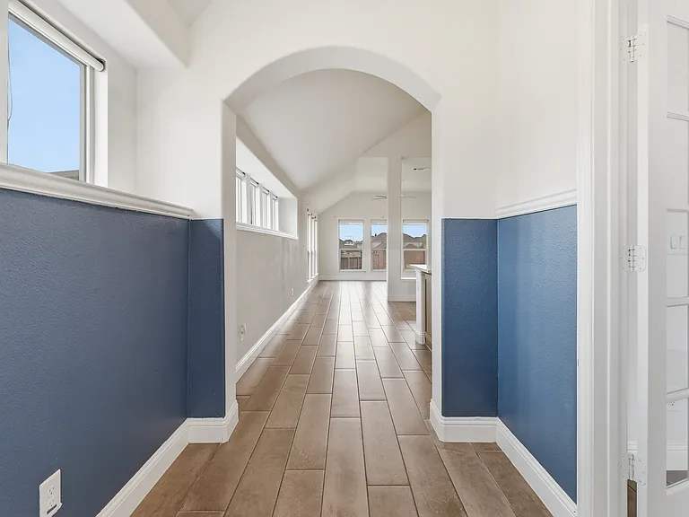 Hallway featuring two-tone walls, wood-finish flooring, an arched entryway, and multiple window installations