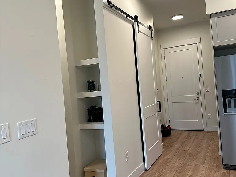 View from living area shows barn door that leads to pantry, shelving in hallway