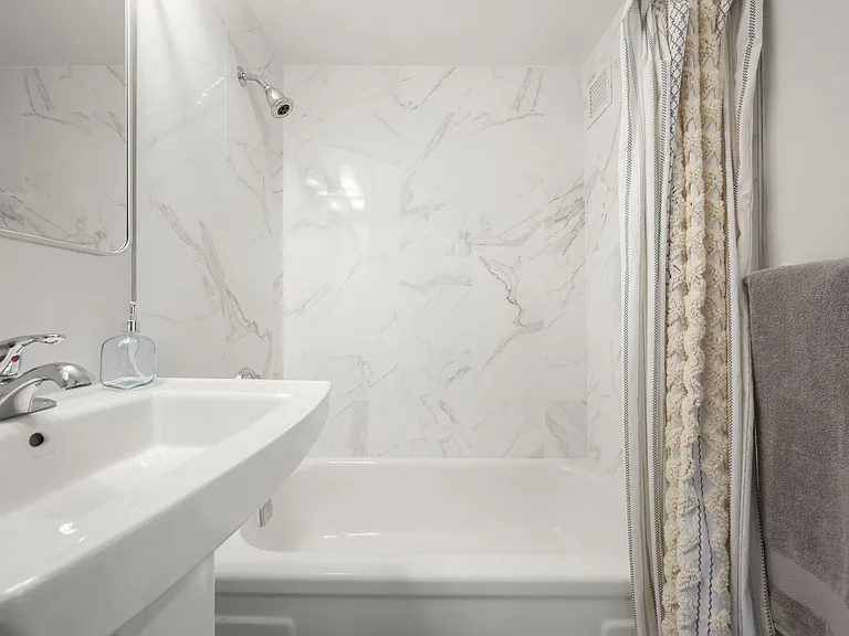 Elegant bathroom featuring a modern tiled bath surround and sleek pedestal sink