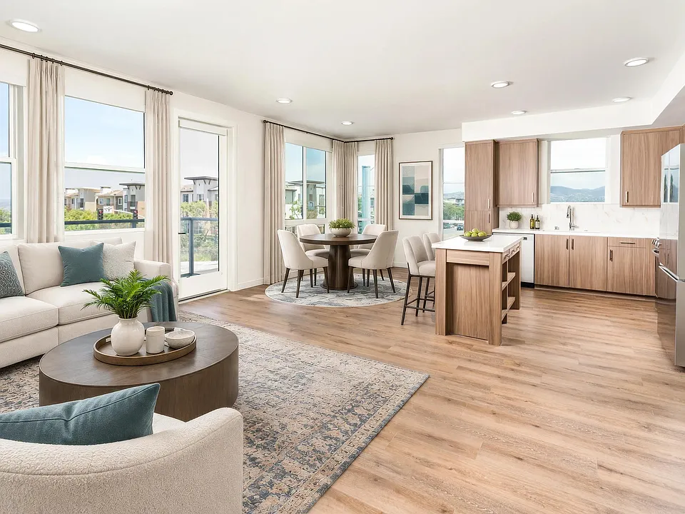 Open kitchen and living area with wood grain cabinetry, sleek surfaces, and expansive corner windows bringing in daylight and framing rolling hillside scenery.