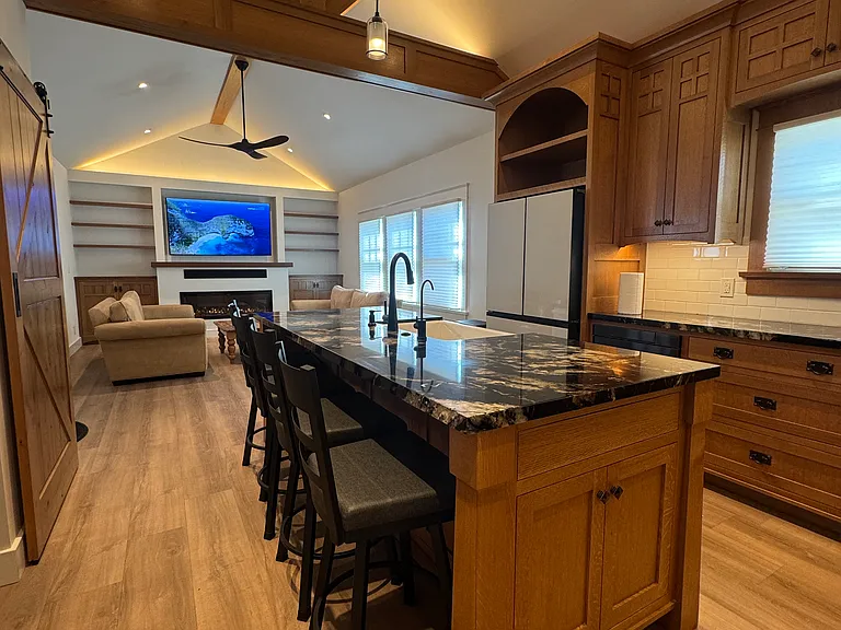 View from back of kitchen to living area with unobstructed view of the TV. Large granite top island with farmhouse sink and Miele dishwasher.