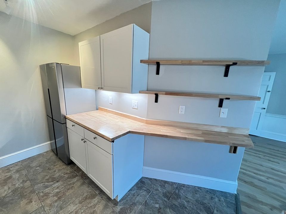 Renovated kitchen with fresh cabinets, butcher block counters, shelving, tiled floors and stainless steel appliances