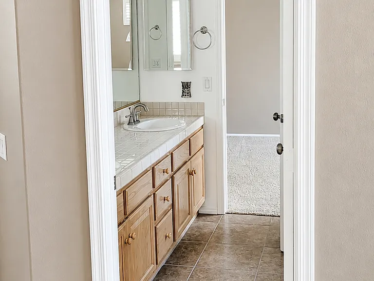 Ensuite bathroom entry with tile flooring, wood vanity, bright white trim, and clean neutral finishes.