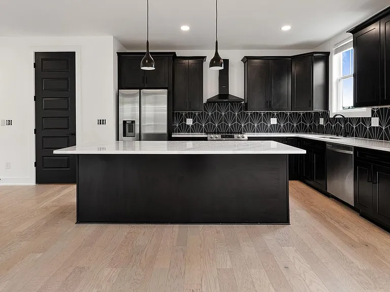 Spacious kitchen with a large island, dark cabinetry, stainless appliances, and a statement tile backsplash.