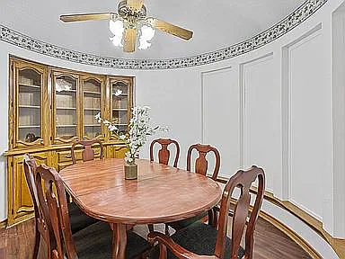 Formal dining area with an oval wood table, matching chairs, built-in display cabinet, and ceiling fan lighting.