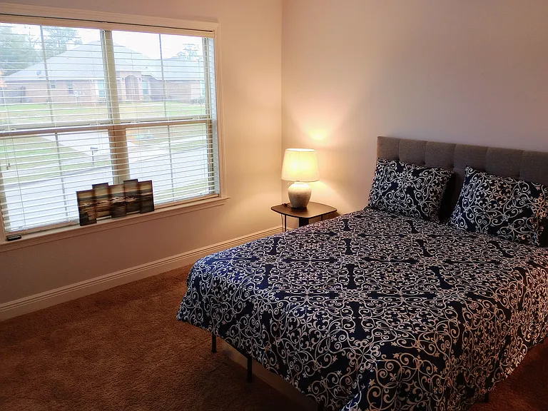 Well-sized bedroom with a large window, plush carpet, and space for a full/queen bed plus a nightstand.