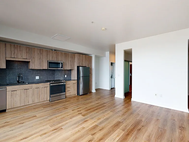 Apartment kitchen with stainless steel appliances, dining and living room with wood-style flooring.