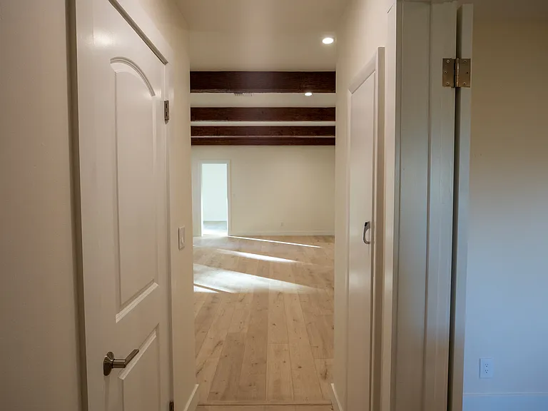Hallway leading to the den. Pantry is on the left with access to the primary bedroom on the right. The door on the right is a hidden ironing board!