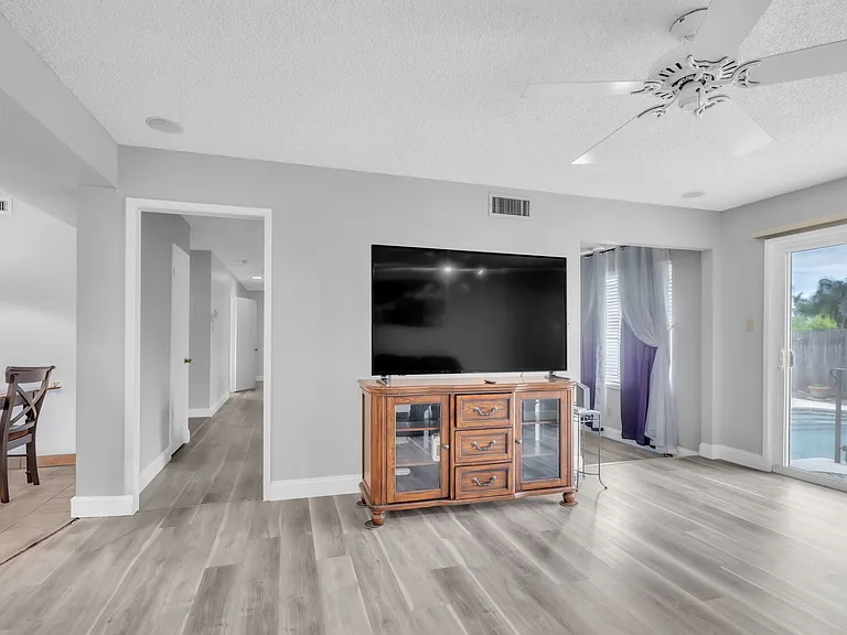 TV, wooden floors in living room. Door going out to the pool.