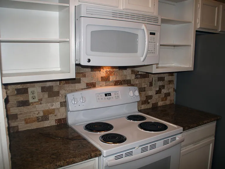 Full size electric range and over-range microwave, granite counter tops, and imported stone backsplash