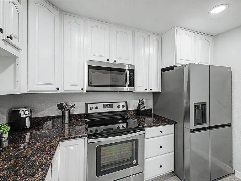 Updated kitchen with ample white cabinetry, dark countertops, and stainless-steel appliances including fridge and range.