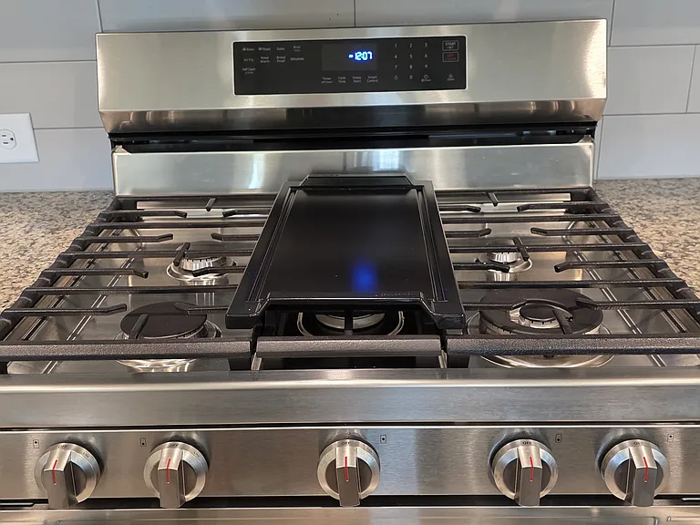 LG 4 burner natural gas stove with center griddle and outdoor vented range hood.
