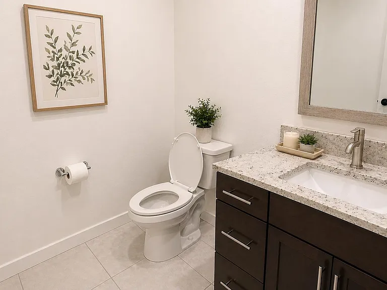 Clean half-bath with granite-style vanity top, ample cabinet storage, and a large framed mirror for easy daily routines.