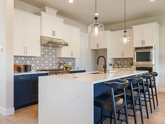 Well-appointed kitchen boasts expansive island with waterfall quartz countertop