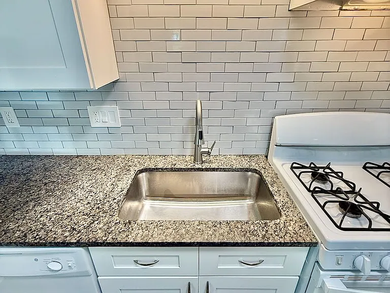 Effortless cleanup station_ - deep stainless sink & pull-down faucet tackle any task with ease - sleek granite counters & tile backsplash turn chores into a stylish ritual