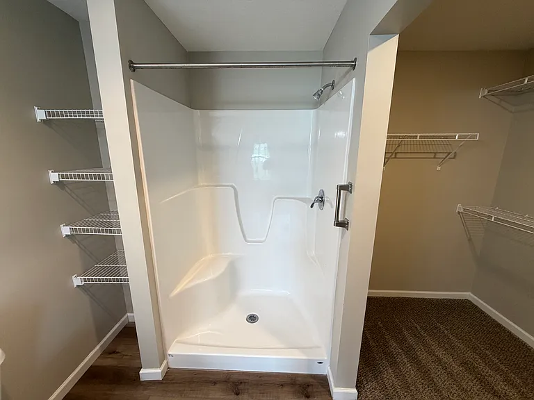 Primary bedroom has a walk-in shower. Shelving for linens on the left and a view of the large walk-in closet on the right.