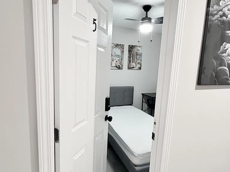 Private bedroom with a comfortable bed, ceiling fan with light, and a small desk area for work or study.