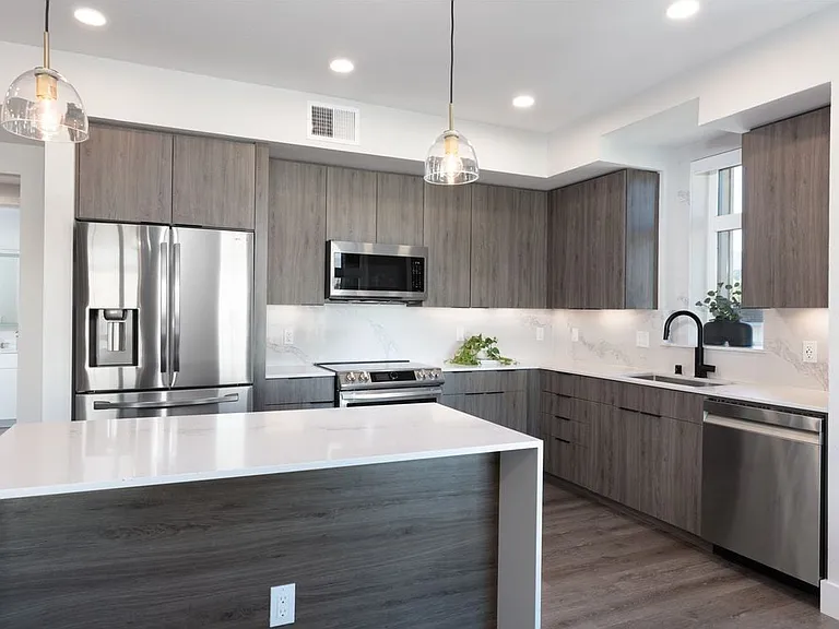 Signature Collection Kitchen with wood cabinetry, marbled quartz countertop and backsplash, upgraded stainless steel appliances, and hard surface flooring