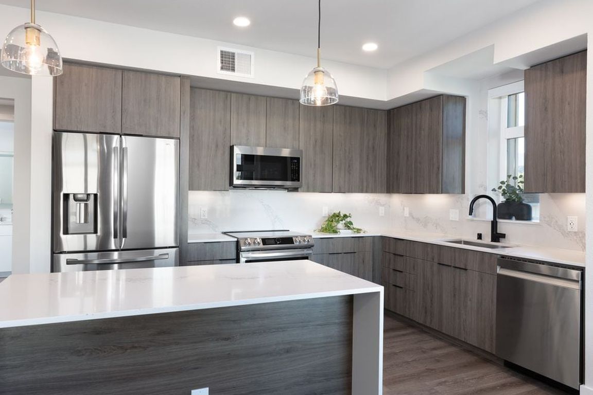 Signature Collection Kitchen with wood cabinetry, marbled quartz countertop and backsplash, upgraded stainless steel appliances, and hard surface flooring