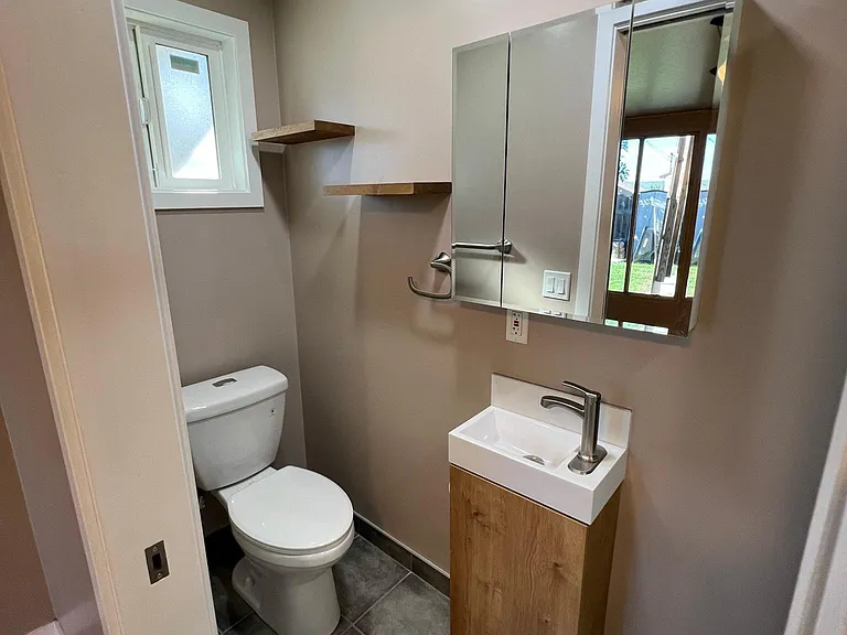 En-suite bathroom with 3-door vanity mirror and floating shelves.
