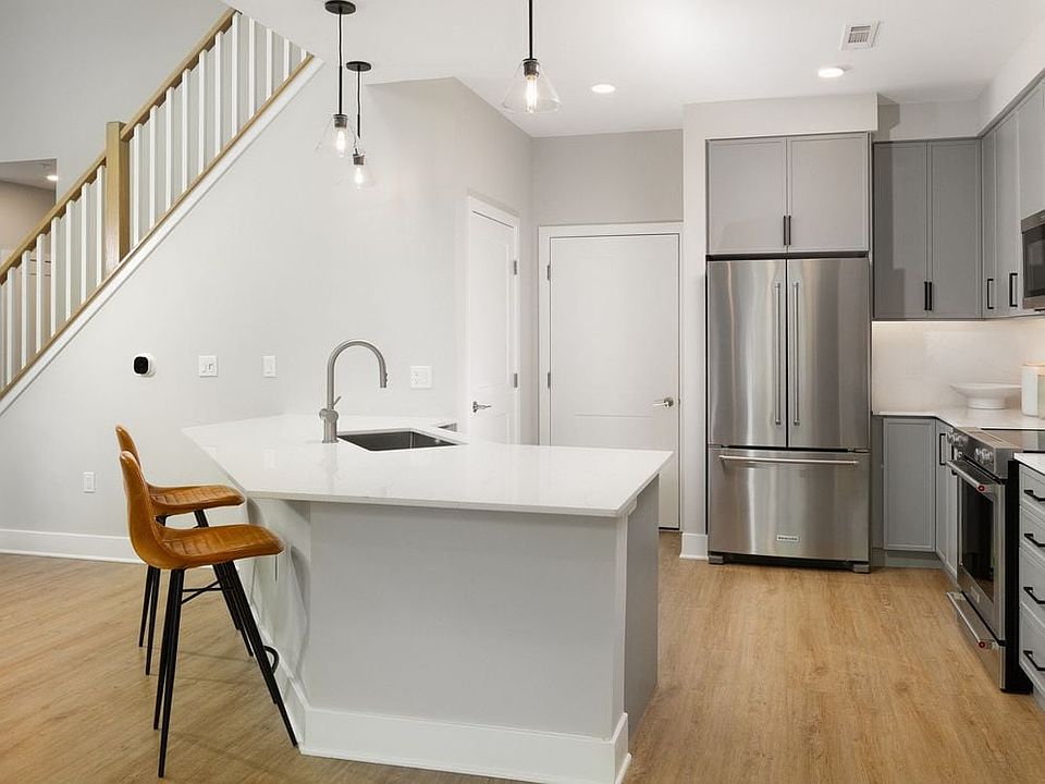Signature Collection kitchen with stainless steel appliances, white quartz countertop, grey cabinetry, white quartz backsplash, hard surface flooring, and pendant lighting