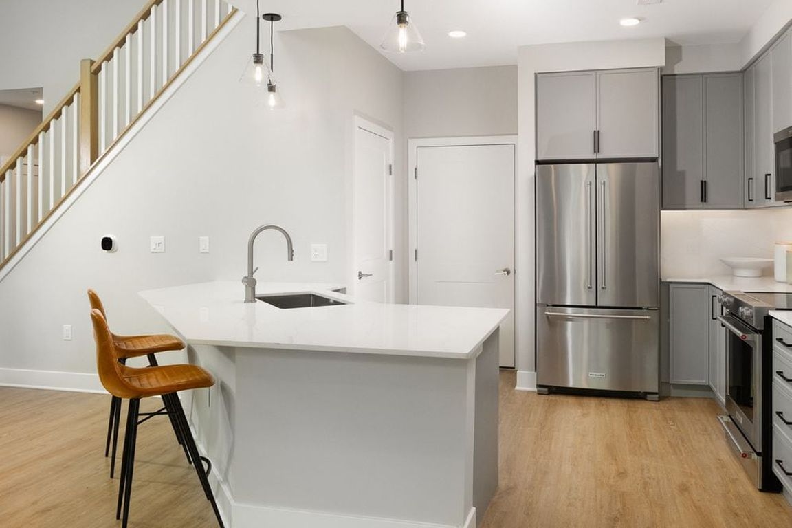 Signature Collection kitchen with stainless steel appliances, white quartz countertop, grey cabinetry, white quartz backsplash, hard surface flooring, and pendant lighting