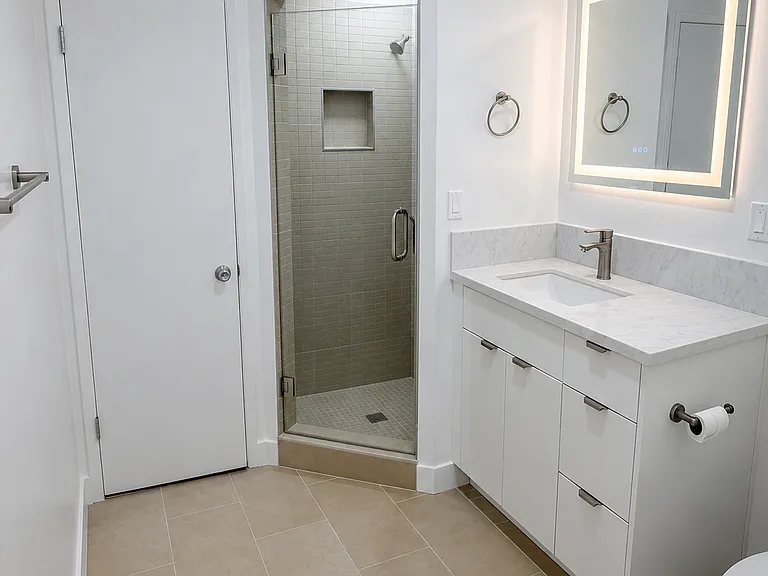 Updated bathroom with modern vanity, illuminated mirror, tiled shower, and clean contemporary finishes.