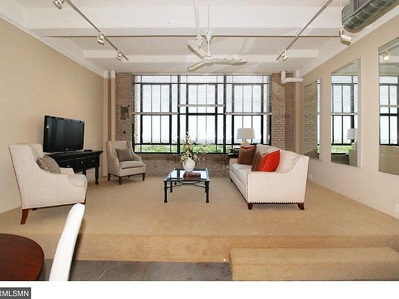 Living room with new carpet, exposed ceiling pipes, and large brick surround window wall