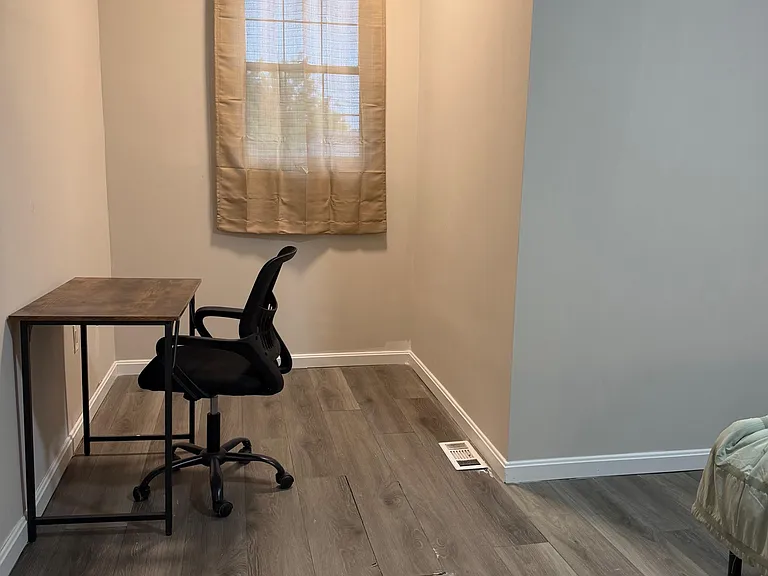 Compact bedroom nook with window and laminate flooring, plus a small desk area for work or study.