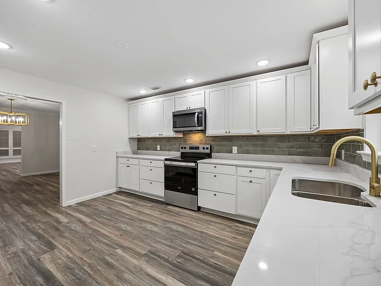 Modern kitchen featuring white shaker cabinetry, stainless steel appliances, a white stone-finish countertop with an undermount sink, and a green subway tile backsplash