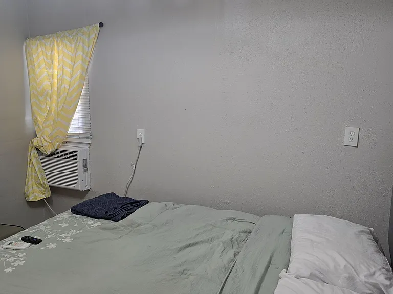 Private bedroom with a furnished sleeping area, window blinds, and in-room window A/C for added comfort.