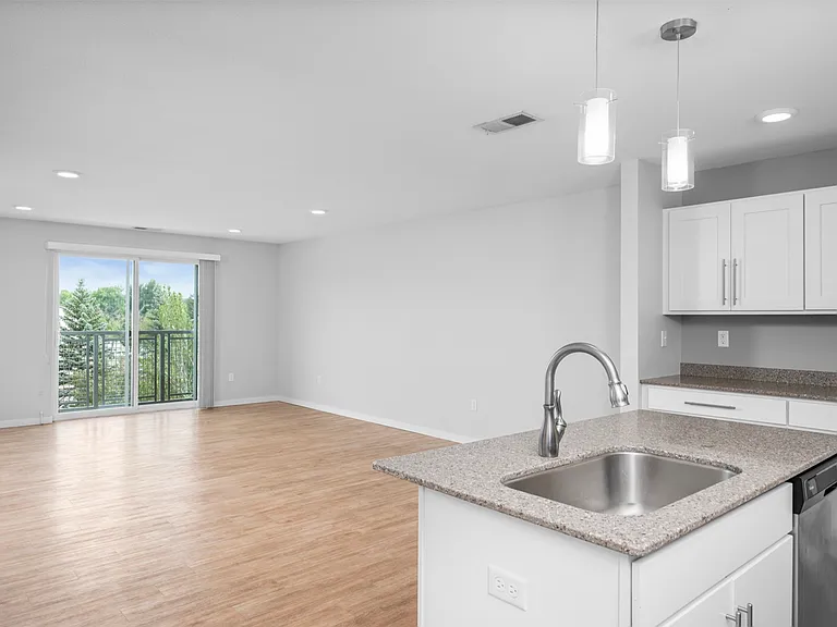 Bright and airy open-concept living area featuring modern kitchen and sleek countertops, with hardwood flooring and large sliding glass doors leading to a scenic balcony view. Bright and airy open-concept living area featuring modern kitchen and sleek cou