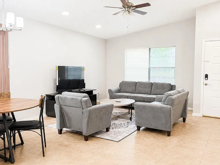 Open living area with a comfortable seating set, TV nook, and adjacent dining space, plus ceiling fan and window blinds.