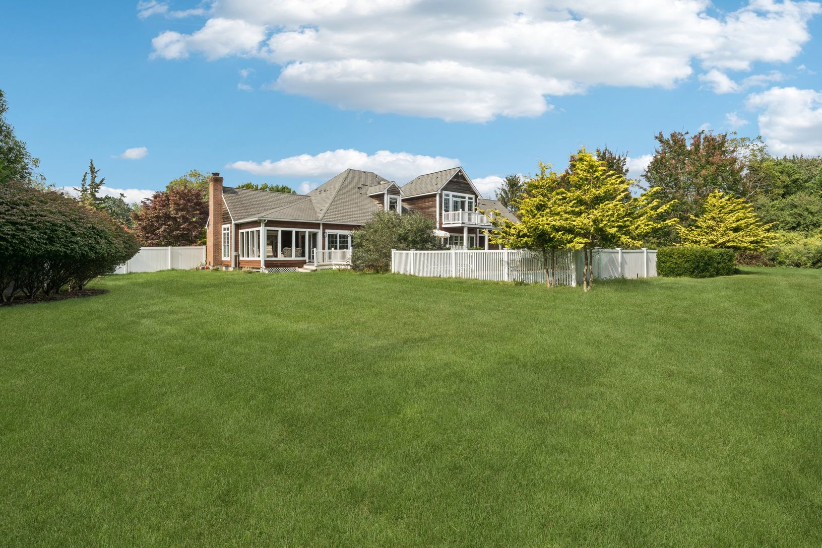 Rear elevation showcasing the home’s fenced backyard, classic chimney, and inviting sunroom.