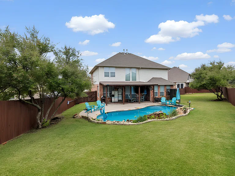 Spacious, fully fenced backyard with a private pool, waterfall feature, shaded patio seating, and lounge chairs. A perfect spot to relax, grill, and enjoy the outdoors.
