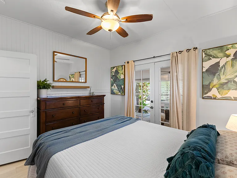 Front bedroom with queen bed, side tables, dresser, AC, ceiling fan, window and large closet with built-in shelving. French doors open to enclosed lanai.