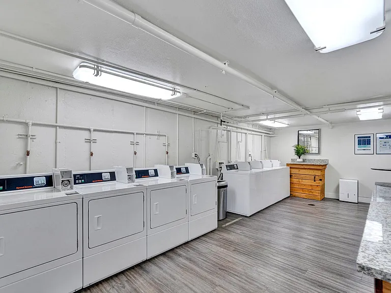 a laundry room with white washers and dryers and a counter with a sink Sunset Station Apartments Portland Oregon