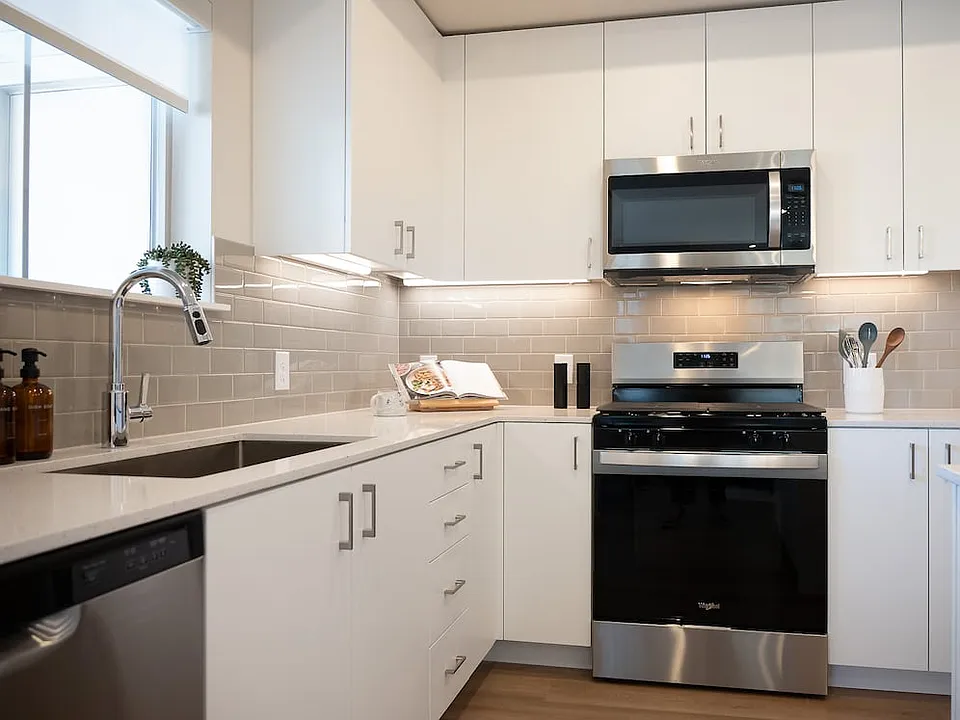 Finish Package I kitchen with stainless steel appliances, white cabinetry, grey tile backsplash, white quartz countertops, and hard surface flooring