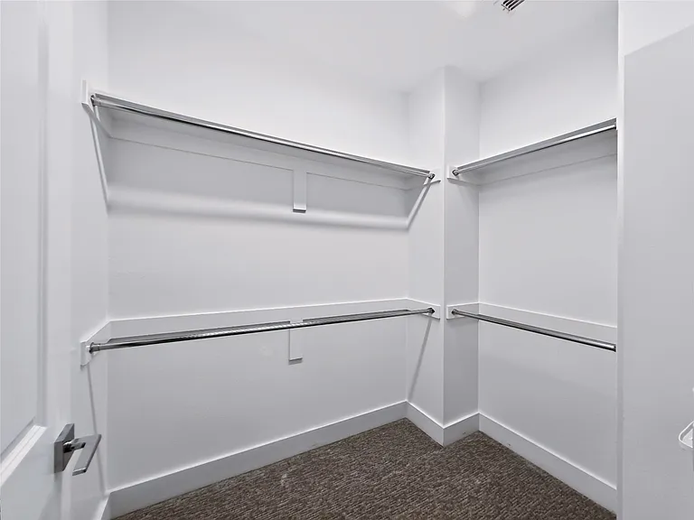 Master Walk-in closet featuring white walls, ample shelving, chrome hanging rods, and dark carpeting