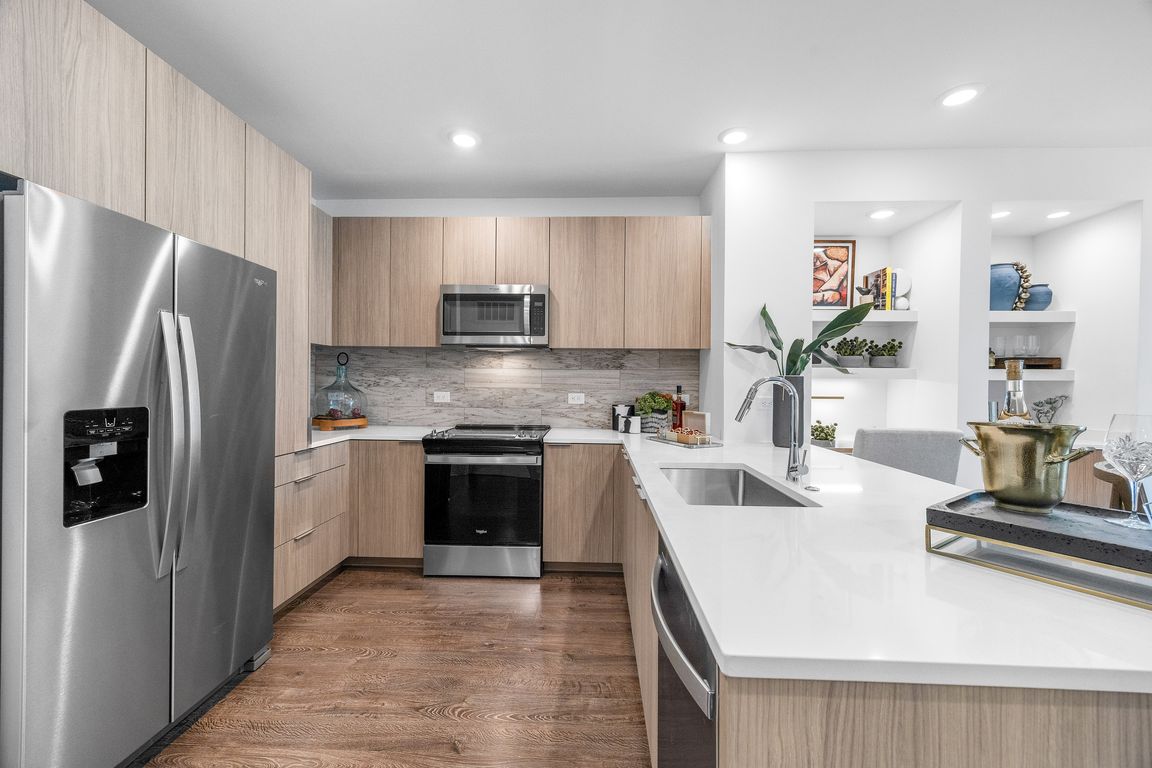 Modern kitchen with sleek appliances, elegant wood cabinetry, and a spacious white countertop with accent decor.
