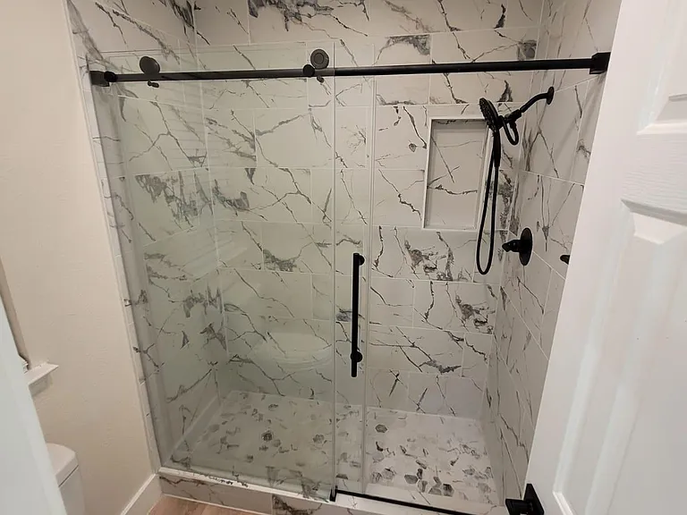 Updated walk-in shower with glass enclosure, marble-look tile surround, and matte black fixtures plus built-in niche.