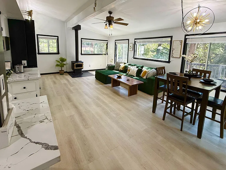 Open-concept living and dining area with a fireplace-style stove, large windows, and direct access to the deck.