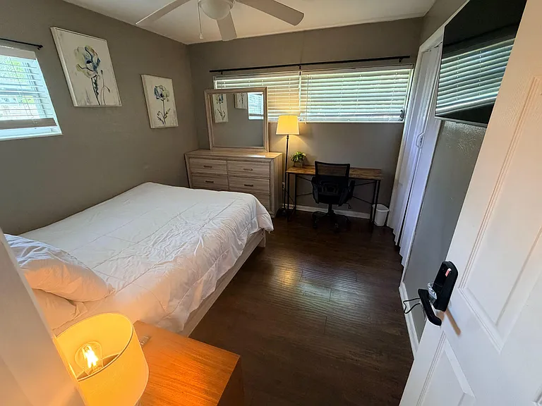 Furnished bedroom, dresser with mirror, and a dedicated desk area, plus windows with blinds & a ceiling fan