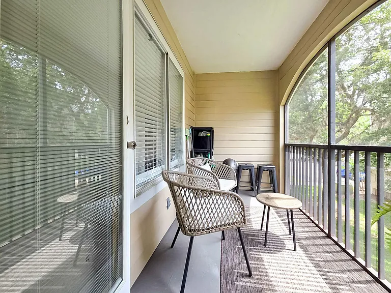 Covered screened balcony with seating, side table, and tranquil tree viewsan ideal spot for outdoor lounging.