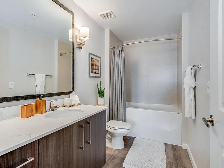 Walk-In Bathroom with Wide Framed Mirror, White Countertop, Tub, and Storage Under Sink