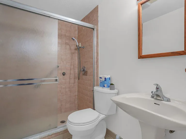 Full bathroom with a tiled shower, sliding glass enclosure, pedestal sink, and wall mirror for daily convenience.