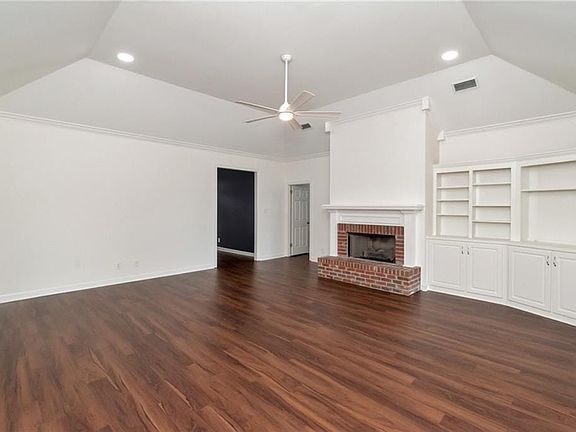 Unfurnished living room featuring visible vents, vaulted ceiling, dark wood finished floors, a fireplace, and a ceiling fan