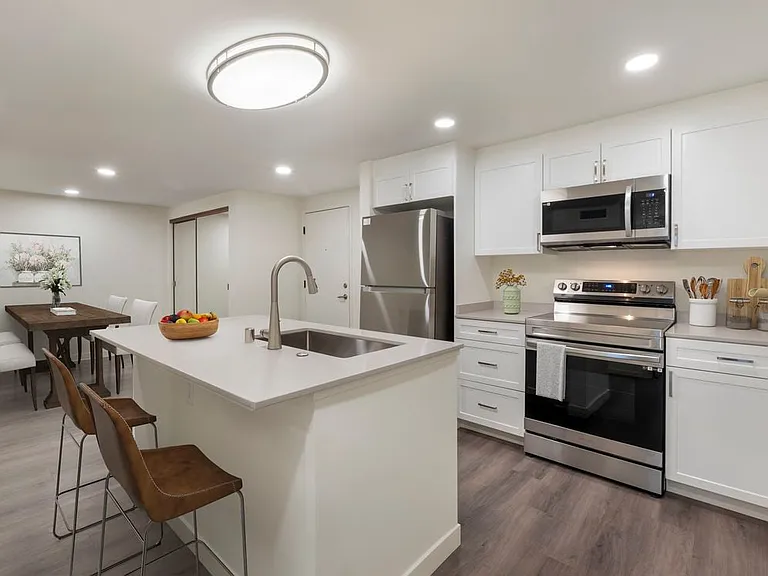 Kitchen with beige quartz countertops, white cabinetry, stainless steel appliances, and hard surface flooring (Select Home)