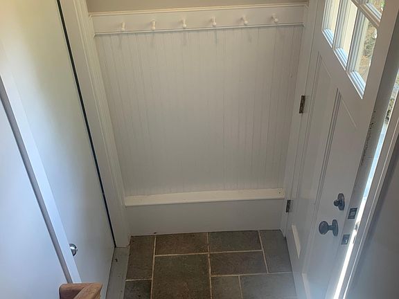 mudroom area with coat hanging rack, fully tiled and wainscoting trim