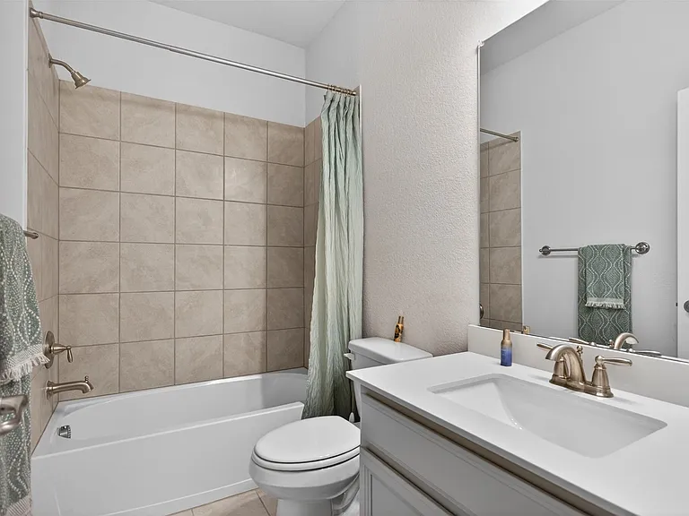 Bathroom featuring a white vanity with an integrated sink, brushed nickel fixtures, a ceramic tile shower surround, and a white bathtub